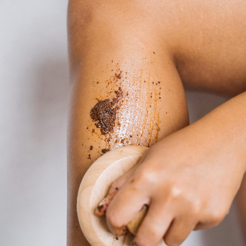 Close-up of a person using a body exfoliator to massage in coffee sugar scrub.